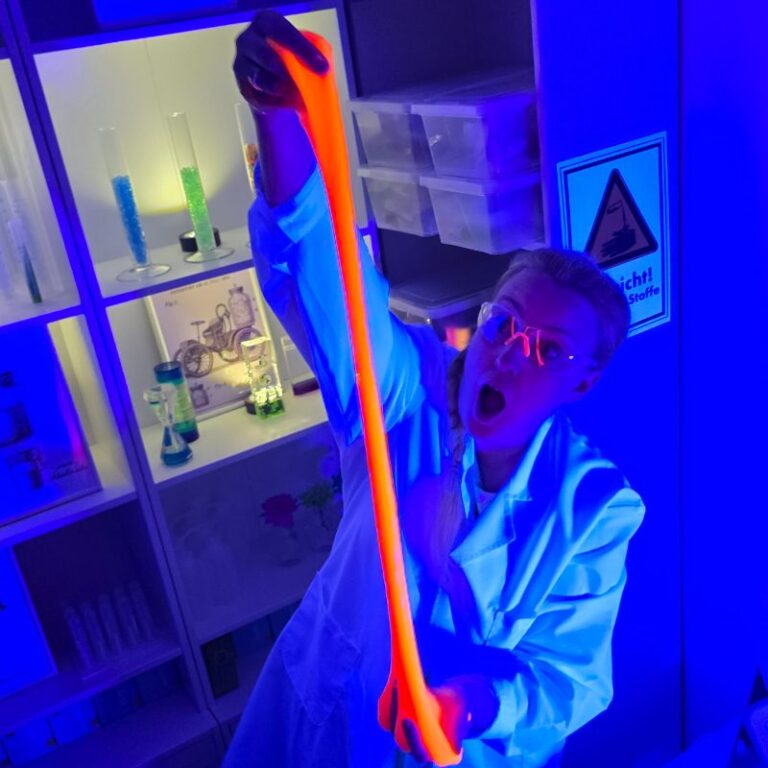 Albertine Schleimstein zieht einen orangen Neon-Schleim in die Länge
